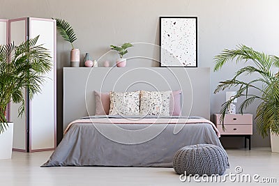 Patterned poster on grey headboard of bed with pillows in bedroom interior with pouf. Real photo Stock Photo