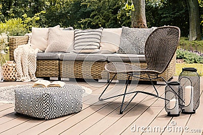 Patterned pouf and rattan chair on wooden patio with pillows on Stock Photo