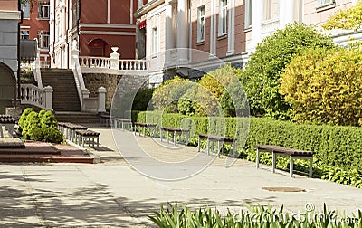 A paved stepped alley trail in a beautiful park framed with cut bushes and benches for rest Stock Photo
