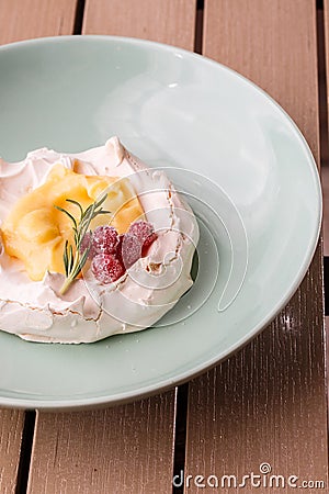 Pavlova mini cake with custard cream and fresh summer berries on green plate on wooden background. Baked meringue cake. Stock Photo