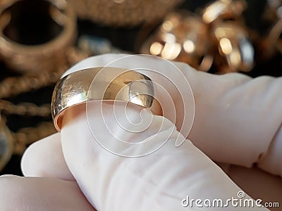 Pawnshop worker verify golden wedding ring on many golden and silver jewelleries and money background. Customers Buy and Sell Stock Photo