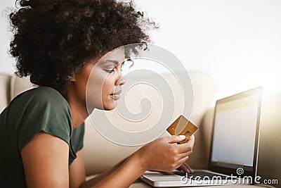 Paying the bills. a woman using her laptop on the sofa at home while holding a bankcard. Stock Photo