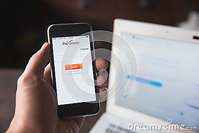 Payoneer on iPhone with computer laptop background. Editorial Stock Photo