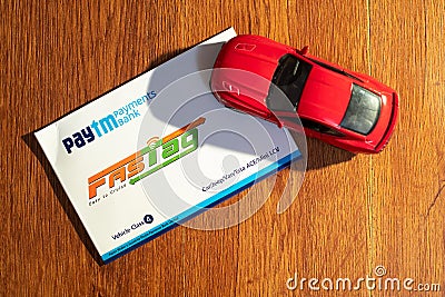 Paytm payment bank issued FASTag RFID contactless cashless payment tag with red model car on a wooden background Editorial Stock Photo