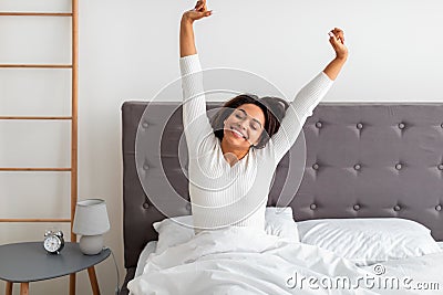 Peaceful black woman stretching arms and back sitting on bed Stock Photo