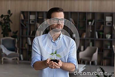 Peaceful businessman hold small green plant look at distance Stock Photo