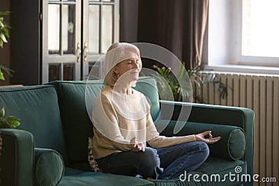 Calm senior woman meditating on couch at home Stock Photo