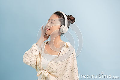 Peaceful good looking magnetic lady standing over blue background, closing eyes, holding headphones, listening to music Stock Photo