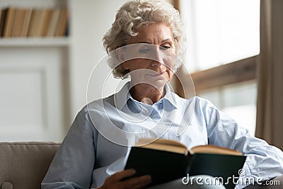 Peaceful older woman reading interesting bestseller paper book. Stock Photo