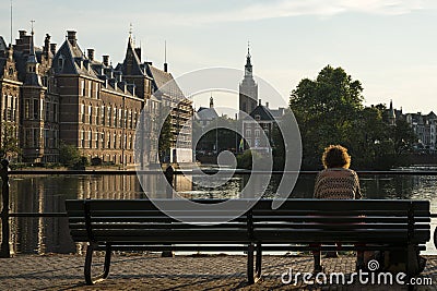 A curly lady sitting on a bench facing the early sunset at Hofvijver pond of The Hague city Editorial Stock Photo