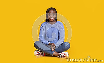 Peaceful woman sitting on floor over yellow studio background Stock Photo