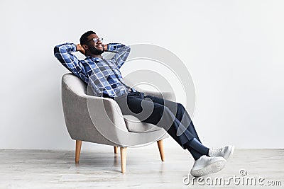 Peaceful young black man relaxing in armchair against white studio wall, free space Stock Photo