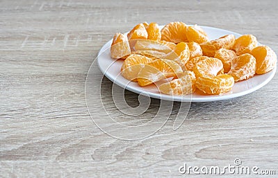Pealed mandarin peaces on white plate, wooden desk surface Stock Photo
