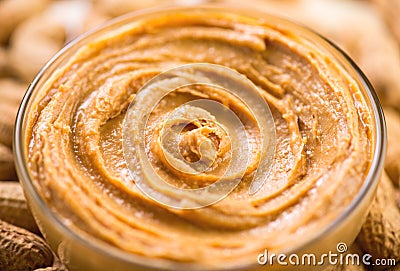 Peanut butter swirls in a glass bowl over raw peanuts background. Creamy smooth peanut butter in jar Stock Photo