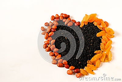 Peanuts, black cumin and raisins are pile all together and make heart shape.eakth and nutrition concept. Stock Photo