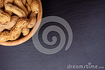 Peanuts lie in a wooden cup on a black stone board in the form of a frame, space for text Stock Photo