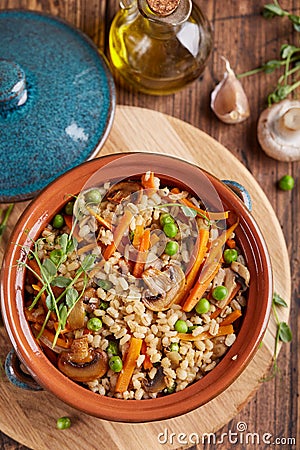 Pearl barley grain porridge with carrot, mushrooms, green peas and onion Stock Photo