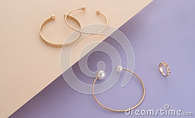 Pearl and diamonds golden bracelets and ring on beige and purple background Stock Photo