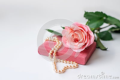 Pearl necklace on rose velvet box and pink one rose. Light background Stock Photo