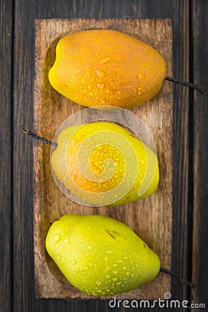 Pears of varying degrees of ripeness in brown craft wooden plate Stock Photo