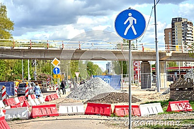 Pedestrian blue road sign and people walking on a sidewalk by a construction site, under a bridge. Editorial Stock Photo