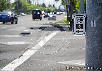 Pedestrian cross walk sign and button on busy street with cars a Stock Photo