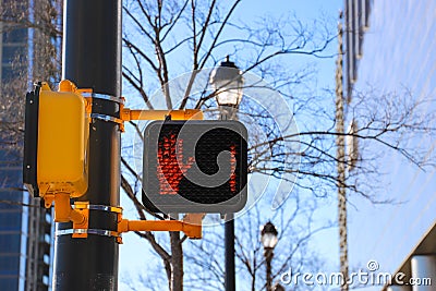 A pedestrian crossing signal with a red hand and a number one attached to a black pole with bare winter trees Stock Photo