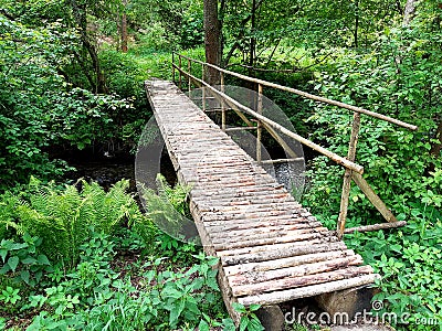 Pedestrian bridge over a stream built of wooden logs with a one-sided railing Stock Photo