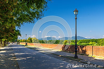 Pedestrian walking path street with lamps on defensive city wall in clear sunny day with Tuscany hills and mountains and clear blu Stock Photo