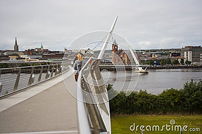 Pedestrians crossing the Derry Peace Bridge towards the walled city Editorial Stock Photo