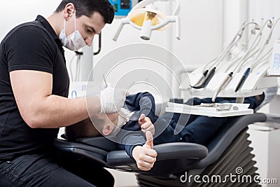 Pediatric dentist examining teeth of boy patient in dental clinic using dental tools. Patient showing thumbs up Stock Photo