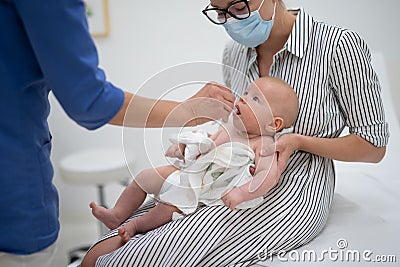 Pediatrician administring oral vaccination against rotavirus infection to little baby in presence of his mother Stock Photo