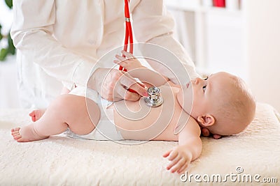 Pediatrician examines baby using stethoscope to listen to baby`s chest checking heart beat. Child is looking at doctor Stock Photo
