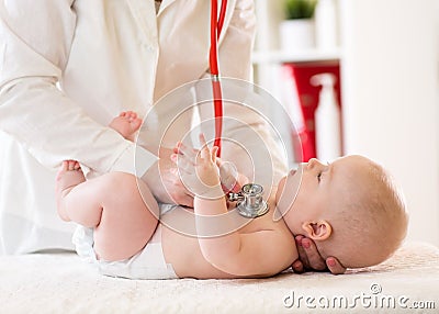 Pediatrician examines five months baby boy. Doctor using stethoscope to listen to child chest checking heart beat Stock Photo