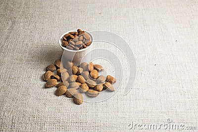 Peeled almonds in a white bowl and almonds nut in shell on beige fabric texture Stock Photo