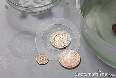 Peeled copper coins lie on the table surface. Corroded coins are lying nearby in a container with phosphoric acid Stock Photo