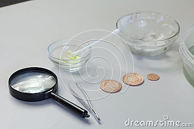 Peeled copper coins lie on the table surface. Corroded coins are lying nearby in a container with phosphoric acid. Sulfuric Stock Photo