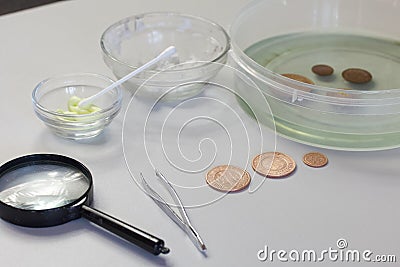 Peeled copper coins lie on the table surface. Corroded coins are lying nearby in a container with phosphoric acid. Sulfuric Stock Photo