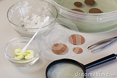 Peeled copper coins lie on the table surface. Corroded coins are lying nearby in a container with phosphoric acid. Sulfuric Stock Photo
