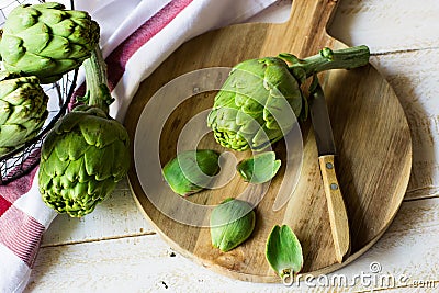 Peeled fresh artichoke preparing for cooking, wood cutting board, knife, vegetables in metal basket, rustic kitchen interior Stock Photo