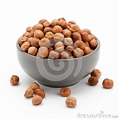 Peeled hazelnuts in a bowl and a few nuts scattered around on a white background Stock Photo