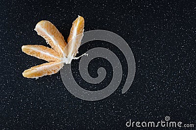 Peeled and sectioned fresh orange on a black cutting board, with pieces missing Stock Photo