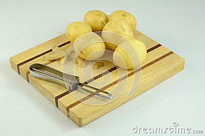 Peeled and unpeeled potatoes with peeler on cutting board Stock Photo