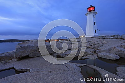 Peggyâ€™s Cove Lighthouse illuminated at sunset with dramatic waves on the foreground, Nova Scotia Stock Photo