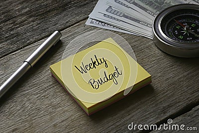 Pen, compass, banknotes and yellow sticky notes written with Weekly Budget on wooden background Stock Photo