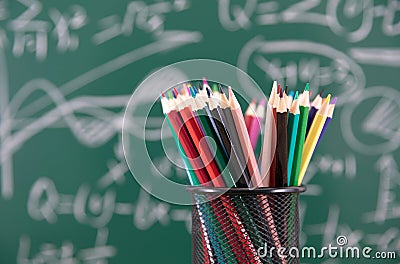 A pen holder filled with colored pencils in front of a blackboard full of mathematical formulas Stock Photo