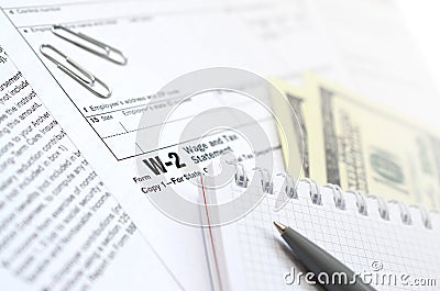 The pen, notebook and dollar bills is lies on the tax form W-2 W Editorial Stock Photo