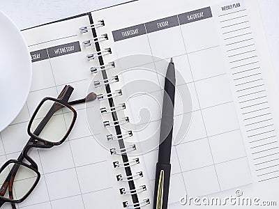 Pen on a page of a weekly plan with glasses on the white office desktop. Stock Photo