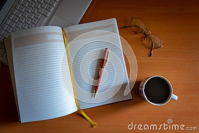 Pencil on a blank journal with reading glasses, cup of coffee and laptop next to it Stock Photo