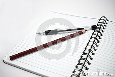 Pencil of brown color and a black color pen placed on top of a white diary Stock Photo